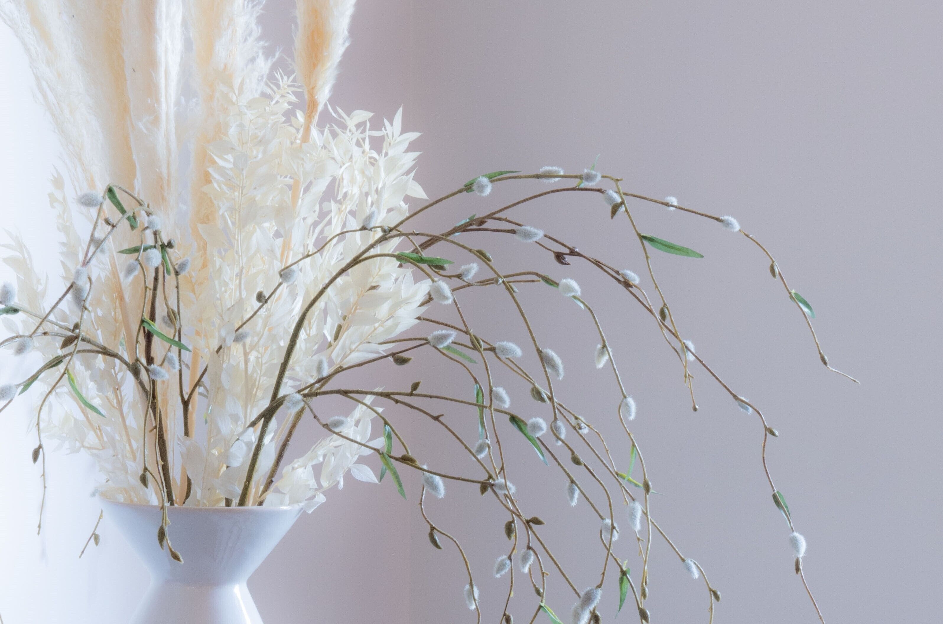 A white vase with a floral arrangement featuring white flowers and green leaves.