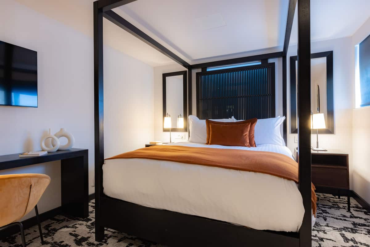 Een moderne hotelkamer met een hemelbed, een bureau met stoel en twee bedlampjes.