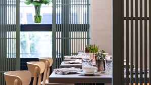 Un coin repas avec des chaises en bois, une table dressée avec des assiettes, des couverts et un verre. Un vase rempli de fleurs est posé sur le rebord de la fenêtre.