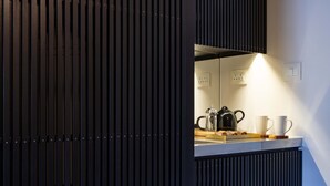 Une cuisine moderne avec un décor de panneaux en bois foncé, un plan de travail sur lequel se trouvent une machine à café, des tasses et une bouilloire.