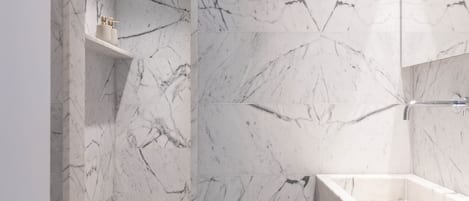 Un baño moderno con paredes de mármol, ducha integrada y tocador con espejo.