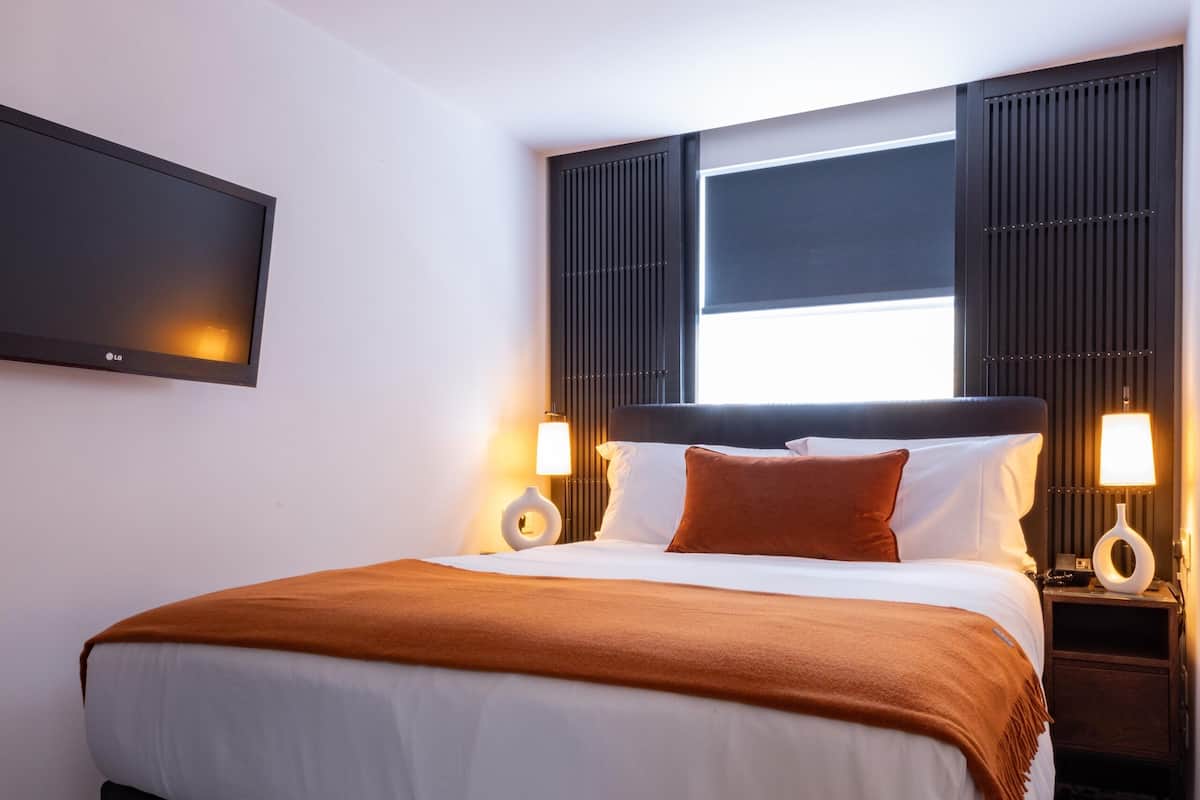 Een moderne hotelkamer met een groot bed, twee nachtkastjes met lampen, een flatscreen televisie en een kamerbreed tapijt met een patroon.