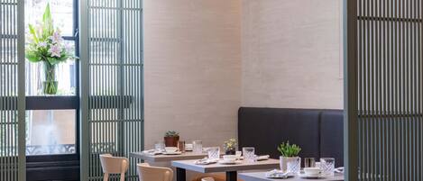 A modern restaurant interior with wooden tables, chairs, and a black cushioned bench.