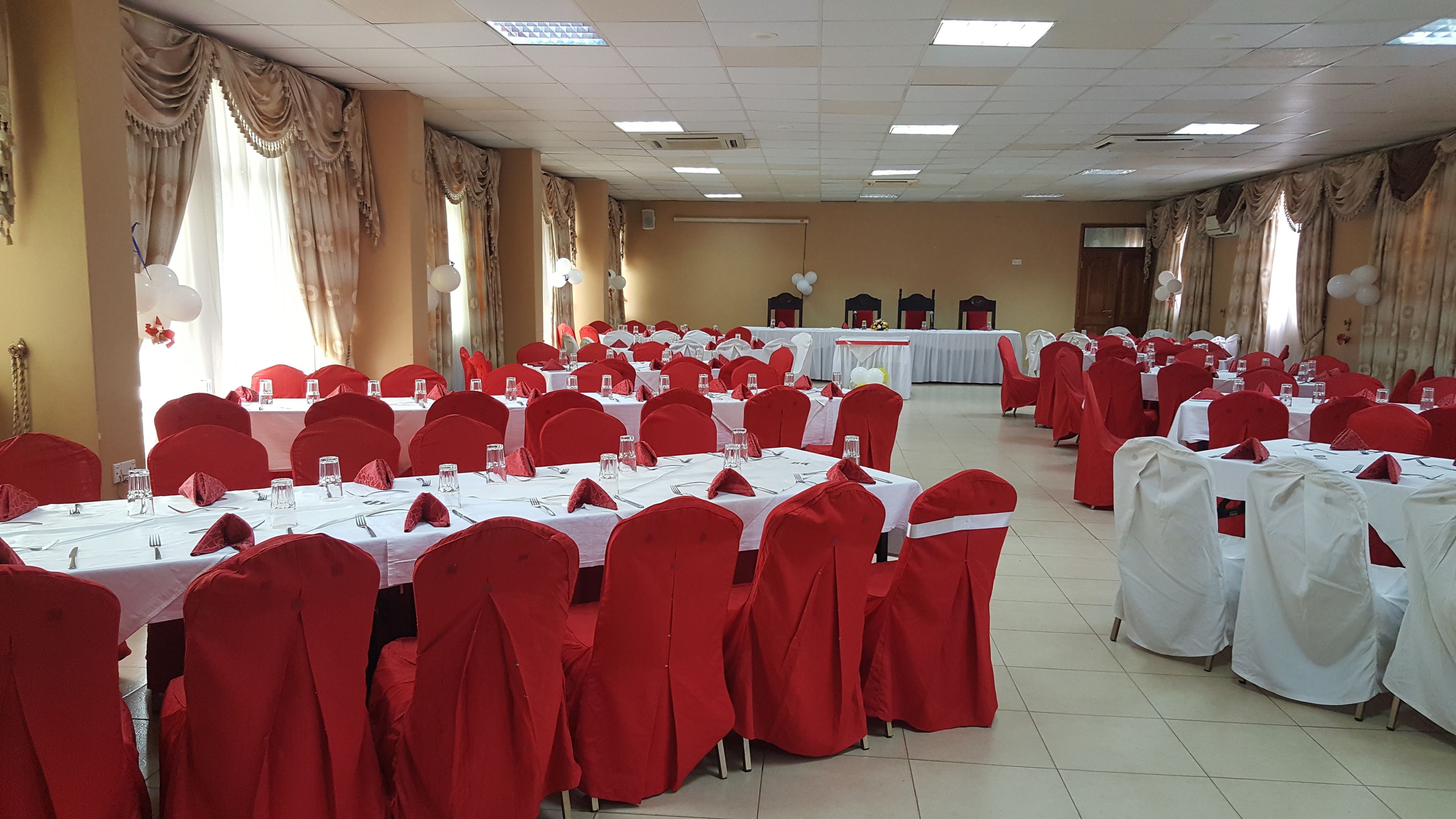 Uma sala de banquetes com fileiras de mesas, cadeiras vermelhas e toalhas de mesa brancas.