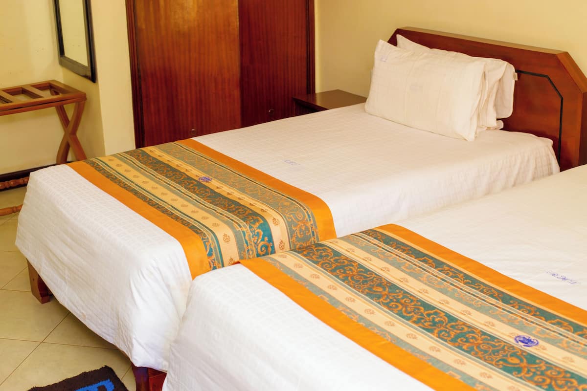 A hotel room with two single beds, wooden headboards, and a wooden wardrobe.