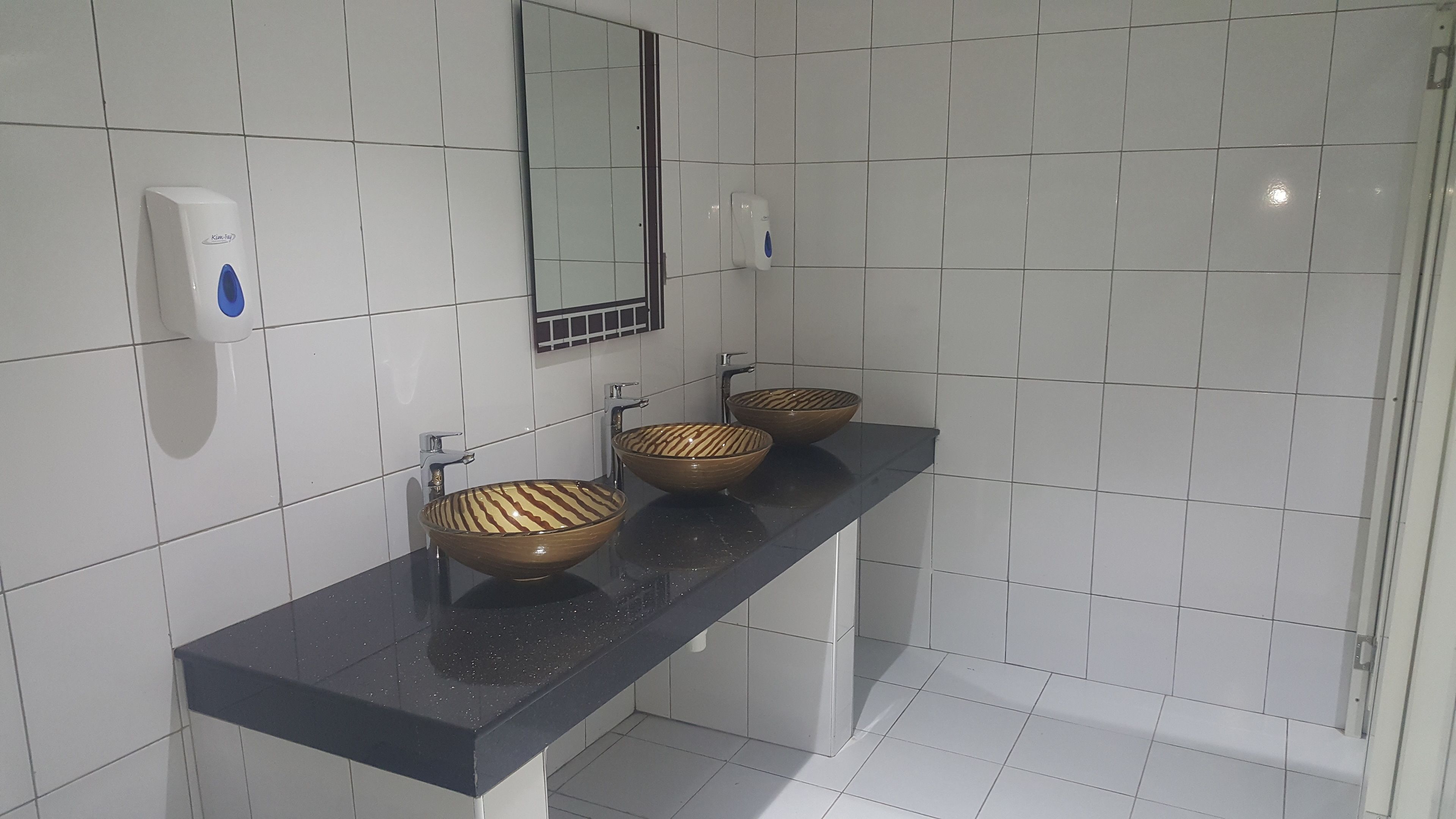 A bathroom with three vessel sinks on a black countertop, a hand soap dispenser, and a mirror above the sinks.