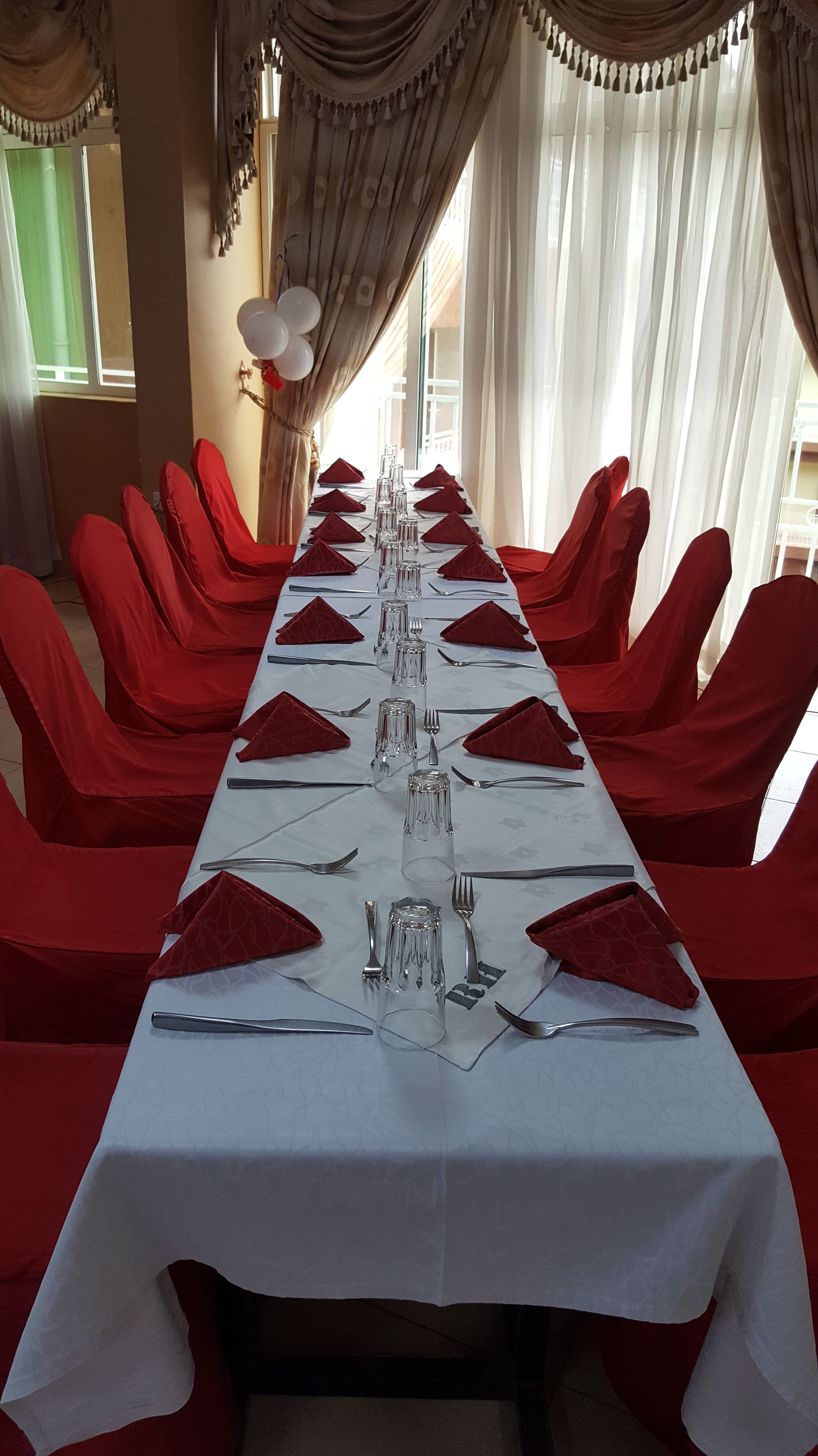 A long banquet table set with red chairs, clear glassware, and silverware, with a white tablecloth.