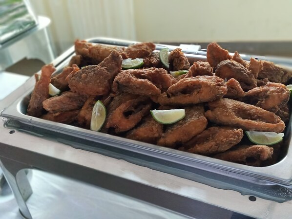 A buffet table with a large container of fried chicken wings garnished with lime slices.