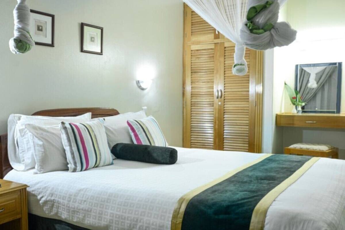A hotel room with a bed, bedside table, and a nightstand. There is a wooden wardrobe with a mirror and a small table with a vase.