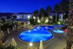 A swimming pool with lounge chairs and umbrellas, surrounded by palm trees and a building with multiple windows. - Mandarin Resort & Spa (Bodrum)