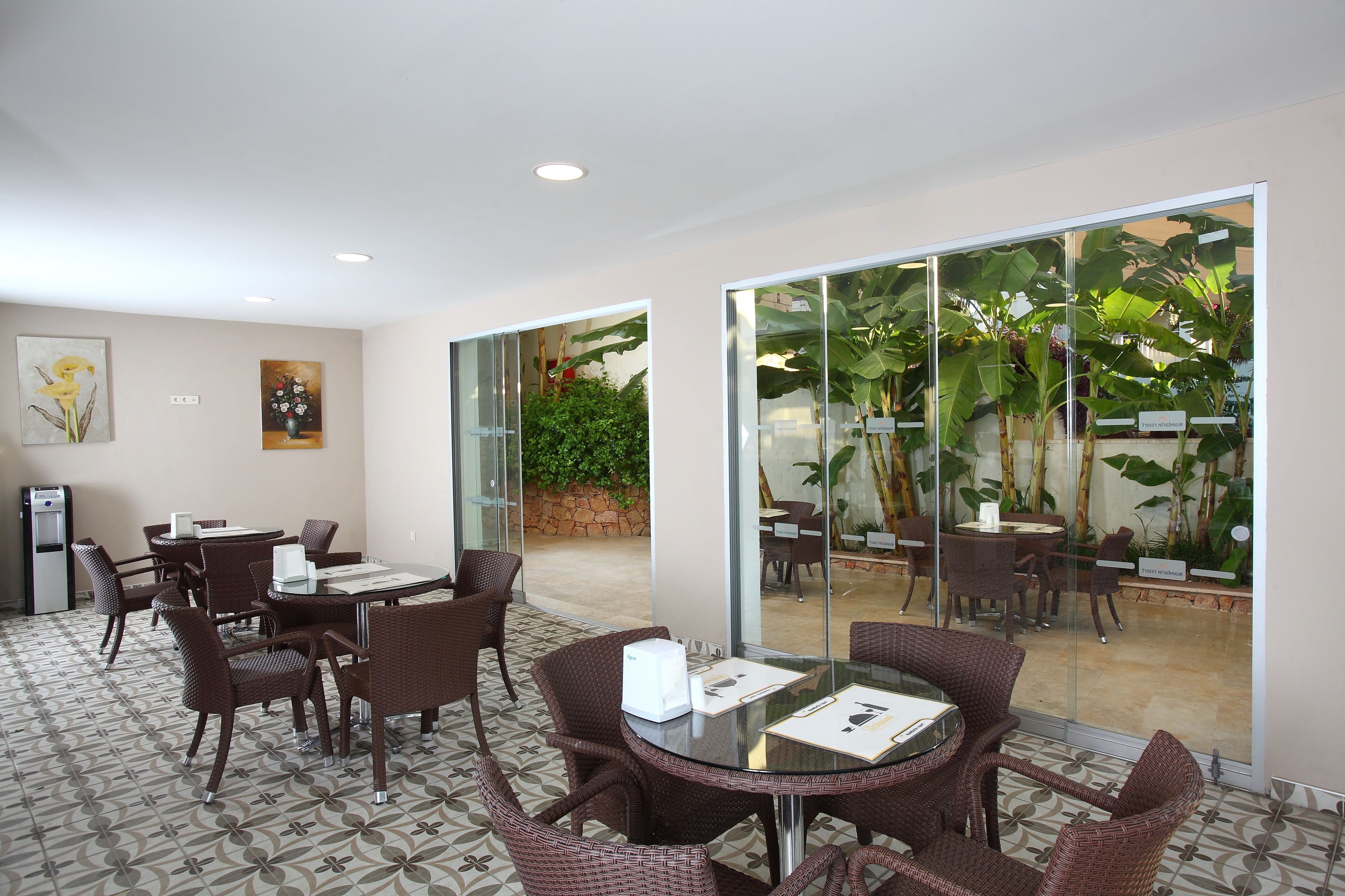 A hotel room with a dining area, a small kitchenette, and a large sliding glass door leading to an outdoor patio with plants.