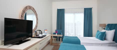 Ein Hotelzimmer mit Flachbildfernseher, Schreibtisch mit Stuhl, Bett mit blauer Bettwäsche und Fenster mit Vorhängen.