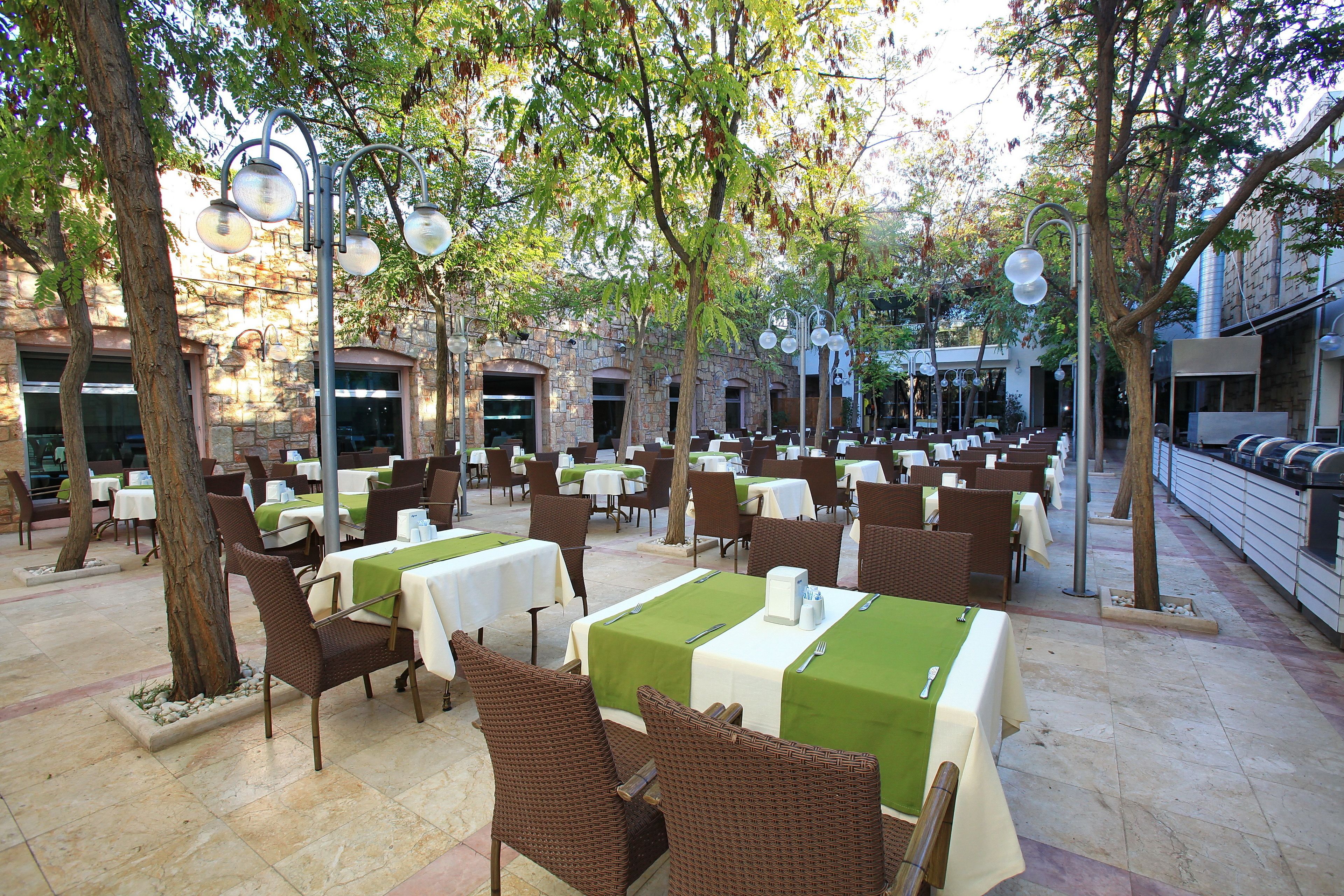 Un espace de restauration en plein air, avec des tables et des chaises, entouré d’arbres et de bâtiments en pierre.