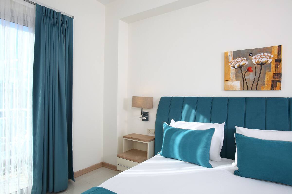 A hotel room with a bed, a nightstand, a lamp, and a painting on the wall.
