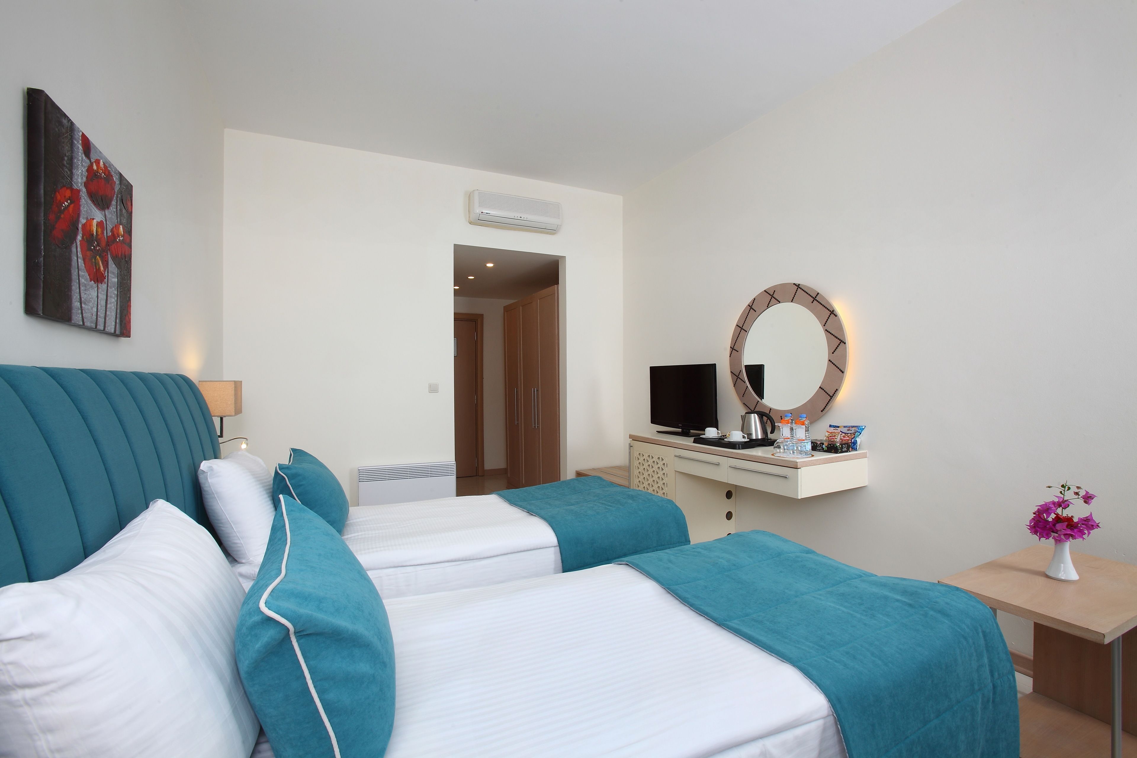 A hotel room with two beds, a desk with a TV, a mirror, and a painting on the wall.