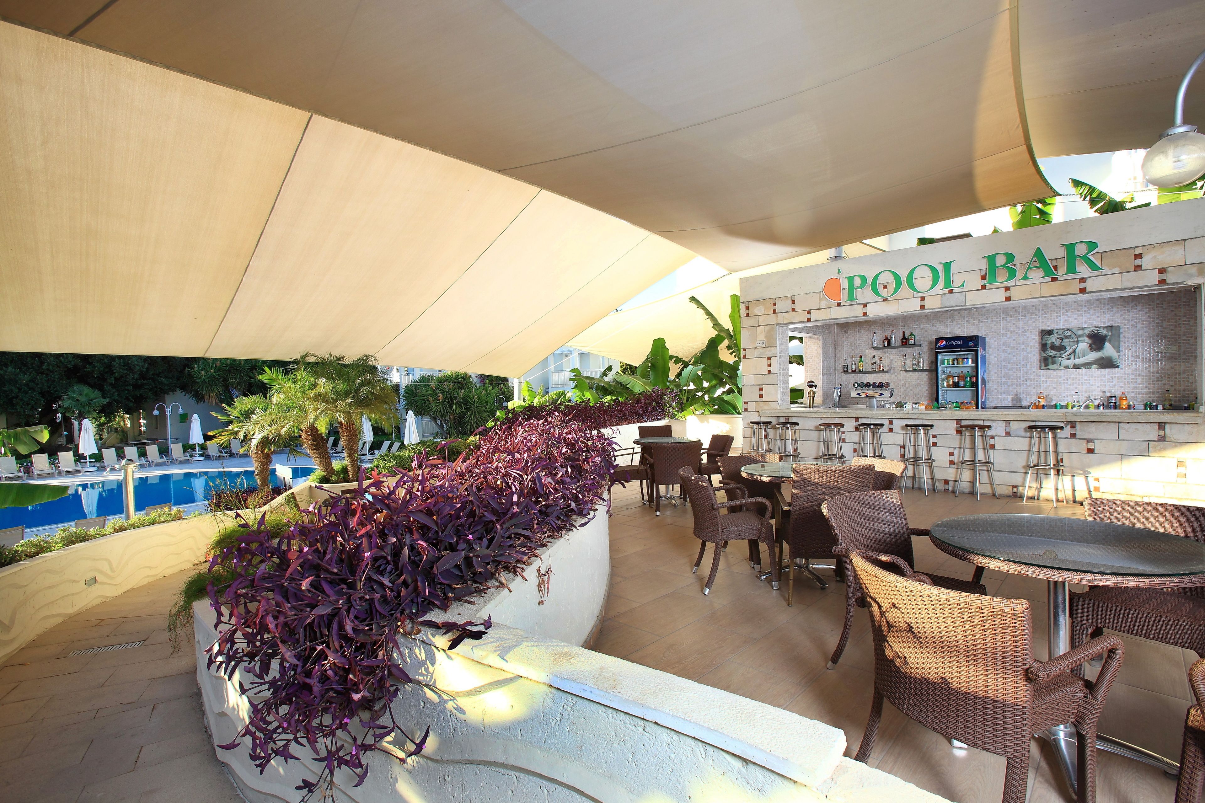 An outdoor pool bar with seating and a bar counter, surrounded by a pool and greenery.