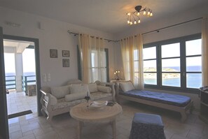 A room with a sofa, a bench, a small table, and large windows with a view of the sea. - Mohlos Villas (Sitia)