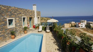 A stone building with a swimming pool, outdoor seating, and a view of the sea. - Mohlos Villas (Sitia)