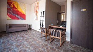 Une pièce comprenant un canapé, une table en bois avec des chaises, un grand tableau abstrait et une porte sombre.