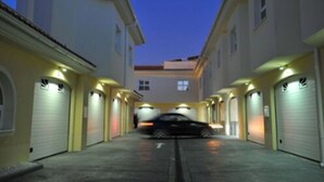 Une rue étroite, bordée de bâtiments des deux côtés, avec une voiture garée au milieu et des portes de garage sur les façades.