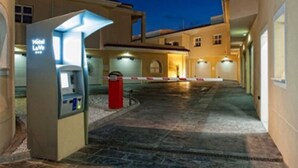 L’entrée d’un hôtel avec un kiosque en libre-service, une allée fermée par un portail et un trottoir dallé.