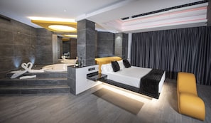 A modern hotel room with a large bed, a separate bathroom with a jacuzzi, and a seating area.