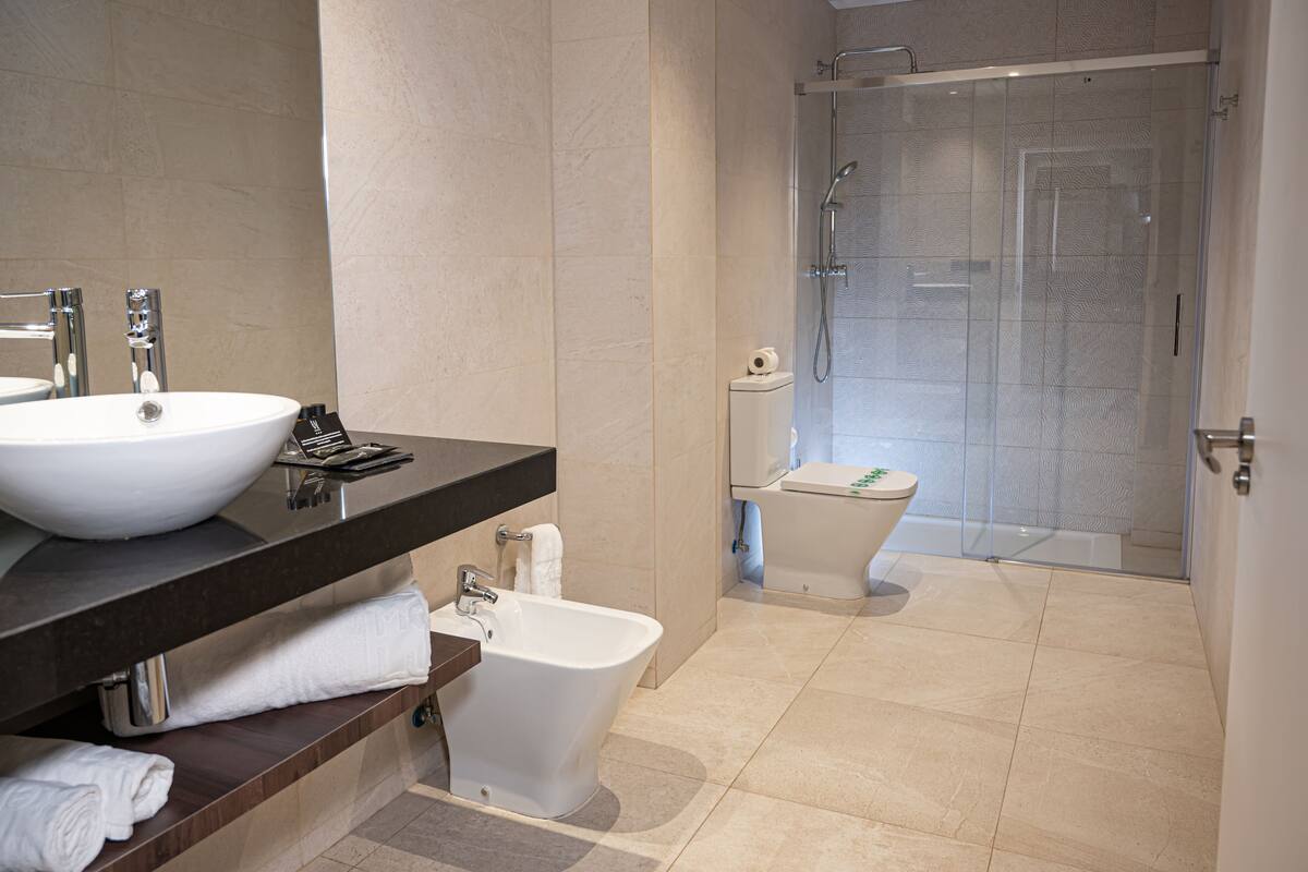 Un baño moderno con un lavamanos grande de color blanco, un bidé y una ducha con cerramiento de vidrio.