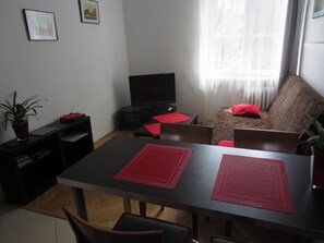 A living room with a dining table, chairs, a sofa, a TV, and a window with curtains. - Unique Warsaw Center Apartment (Warsaw)