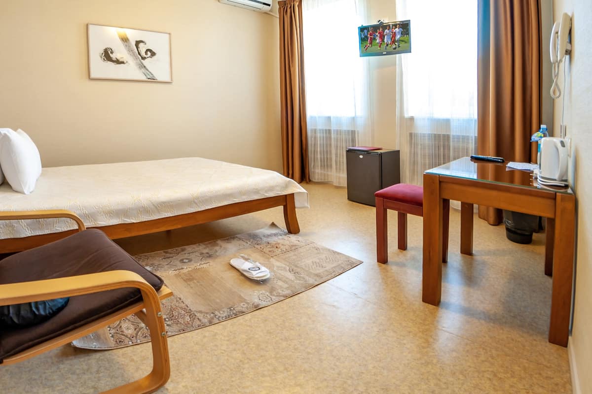 Ein Zimmer mit einem Bett, einem Sessel, einem kleinen Tisch, einem Fernseher und einem Fenster mit Vorhängen.
