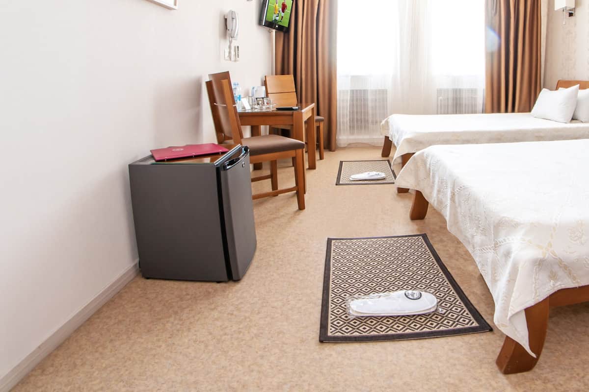 Ein Hotelzimmer mit Schreibtisch, zwei Betten, einem Kühlschrank und einem Fernseher.