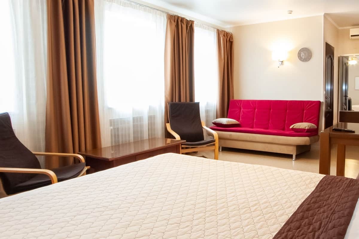 Ein Hotelzimmer mit einem großen Bett, einer roten Couch, einem Holztisch und einem Stuhl.