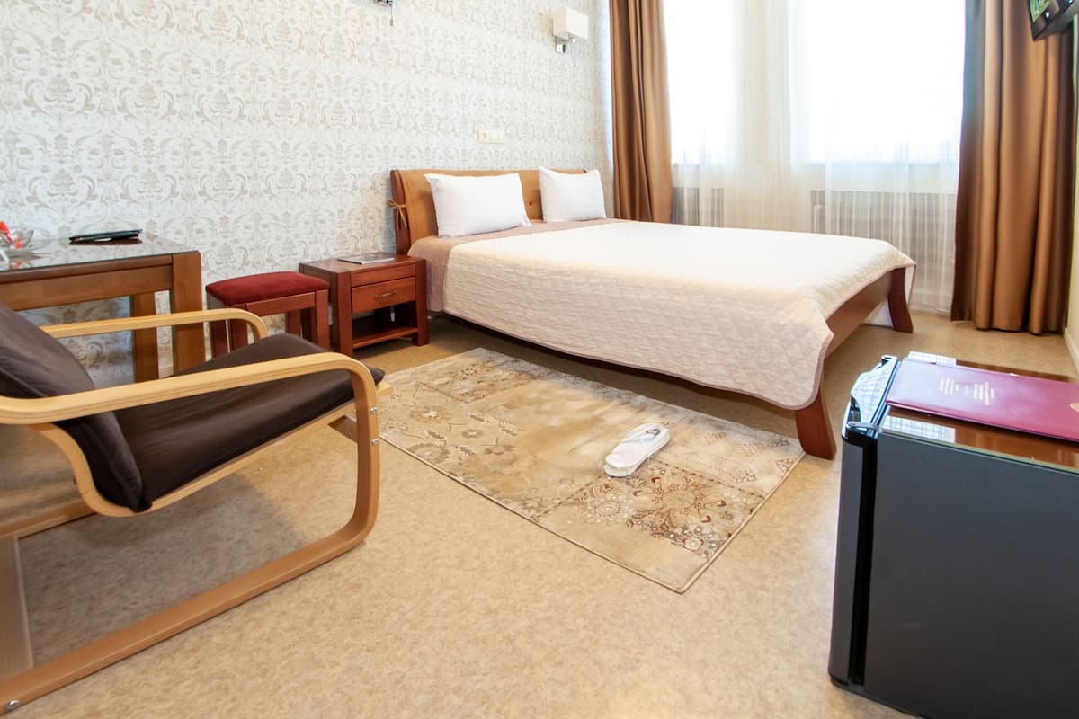 Ein Hotelzimmer mit Bett, Schreibtisch, Stuhl, Nachttisch, Fernseher und Teppich.