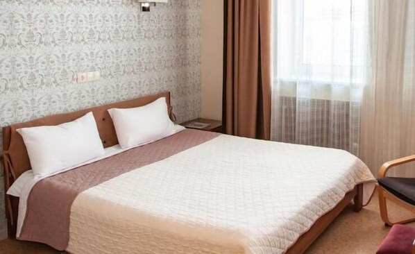 A hotel room with a bed, a nightstand, a chair, and a window with curtains. - Antwo-Hotel (Kharkiv)