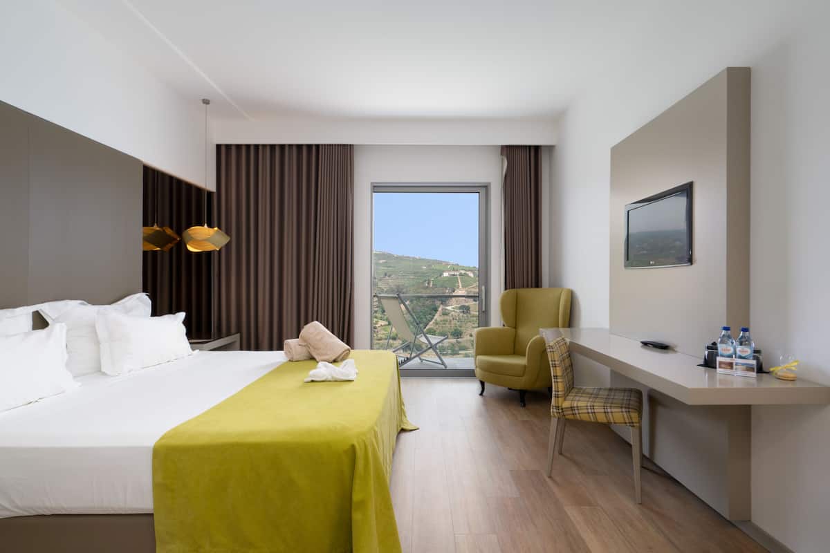 A hotel room with a bed, a desk, a chair, a window with a view, and a mounted TV.