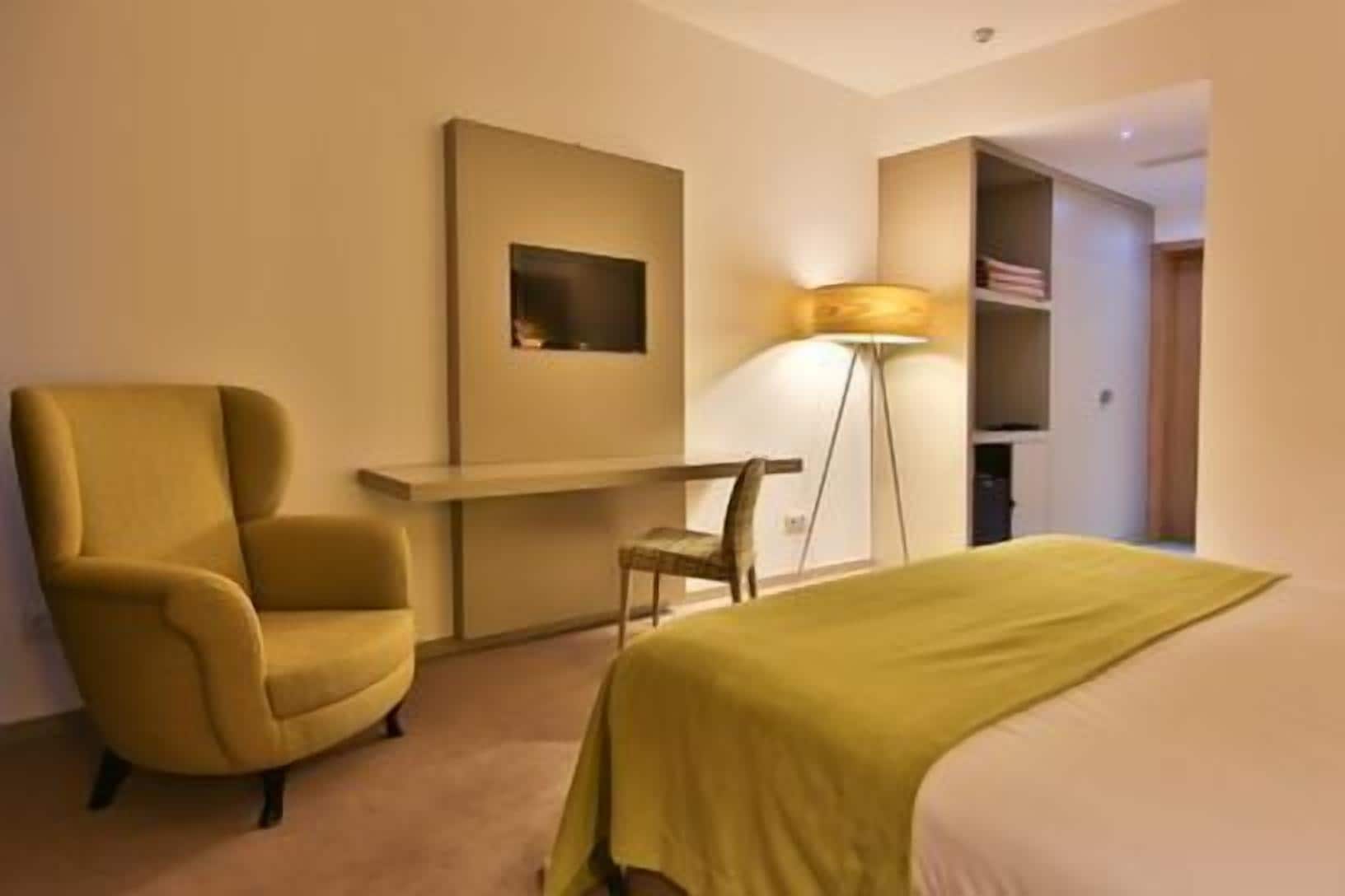 A hotel room with a bed, a desk, a chair, and a lamp.