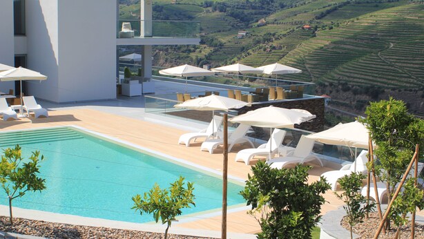 A modern outdoor pool area with lounge chairs and umbrellas, overlooking a scenic hilly landscape. - Delfim Douro Hotel (Lamego)