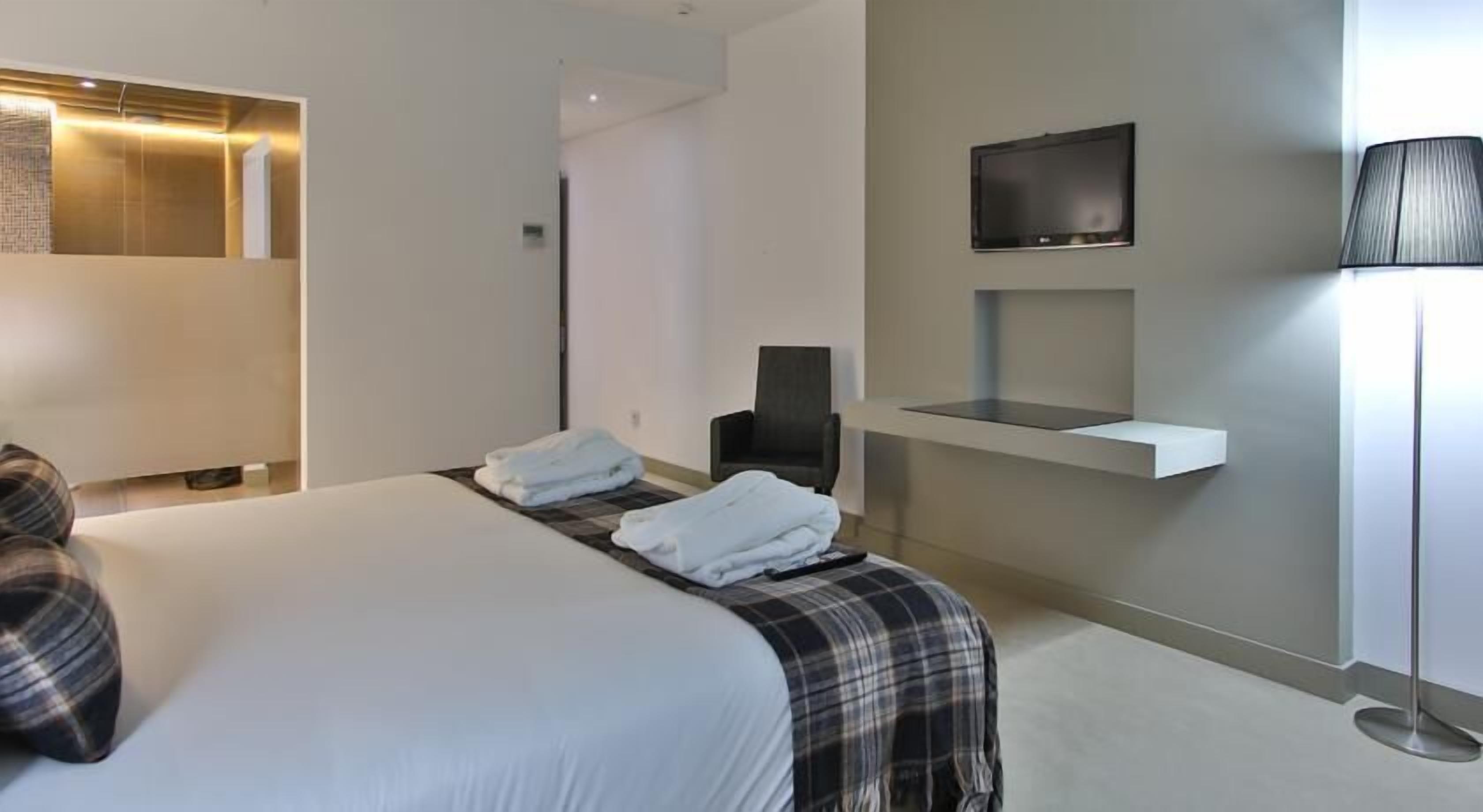 Habitación de hotel moderna con una cama grande, un televisor de pantalla plana montado en la pared, un escritorio pequeño y una silla.