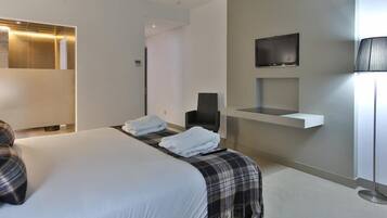 Habitación de hotel moderna con una cama grande, un televisor de pantalla plana montado en la pared, un escritorio pequeño y una silla.