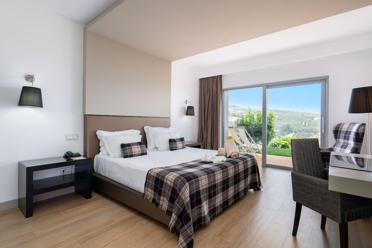A modern bedroom with a large bed, a desk, and a view of the outdoors.