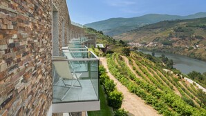 A modern building with a brick facade and a glass balcony overlooking a vineyard and river. - Delfim Douro Hotel (Lamego)