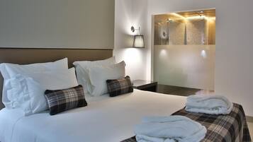 Habitación de hotel con una cama grande, dos almohadas, una mesita de noche y un aplique de pared.