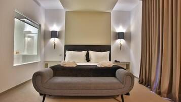 Une chambre d’hôtel moderne avec un grand lit, deux lampes de chevet, un canapé, un grand miroir et une vue sur la ville.