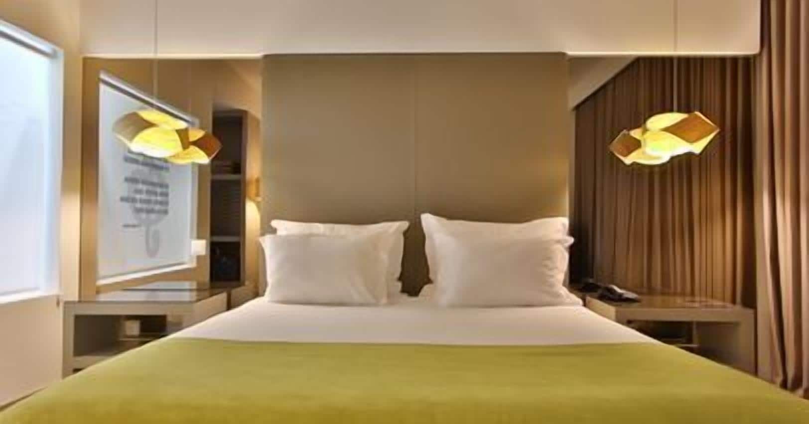 A hotel room with a large bed, two bedside tables, and a headboard with integrated lighting.