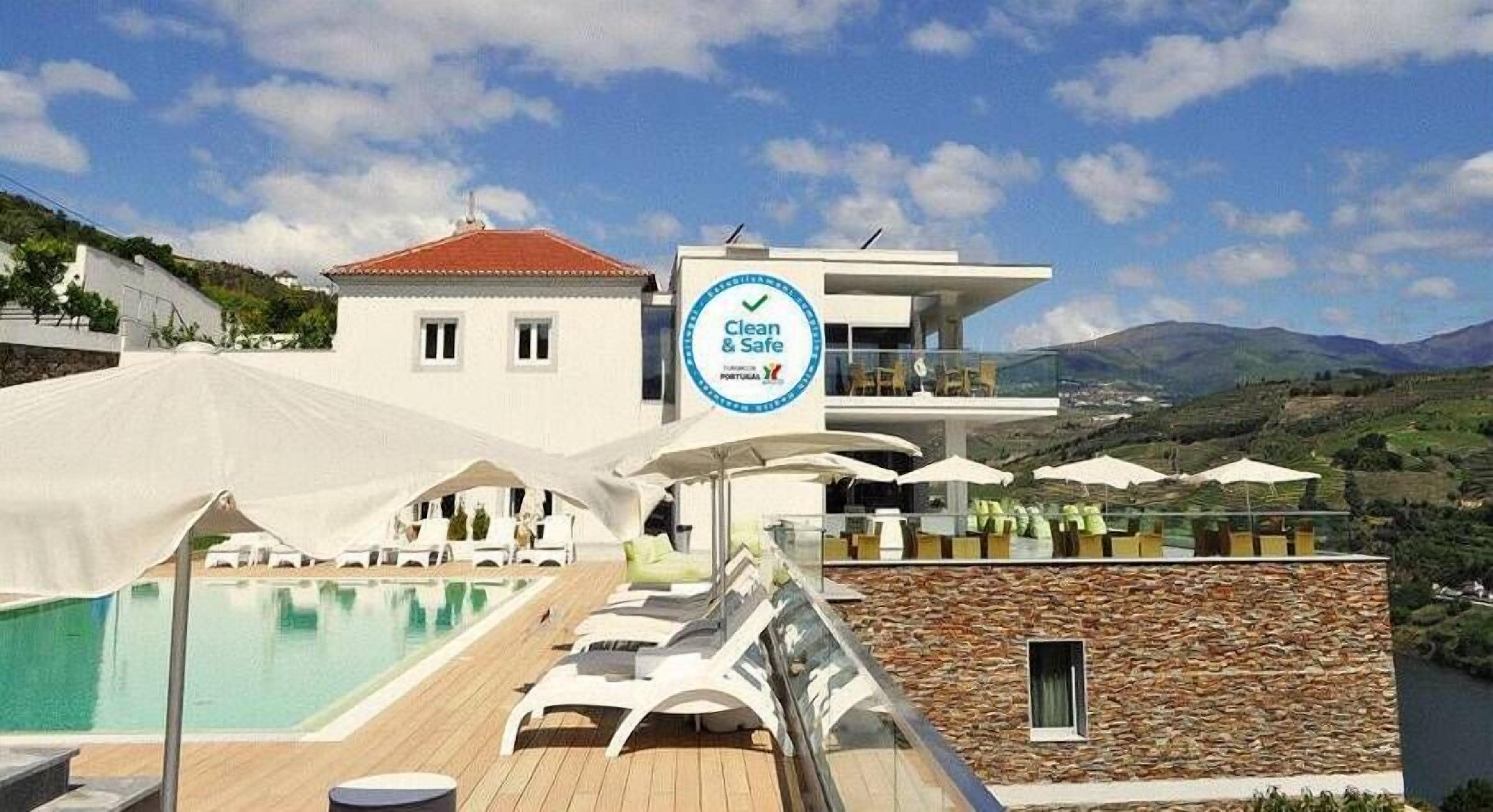 A modern hotel with a pool area, a sign indicating 'Clean & Safe', and a view of the surrounding landscape.