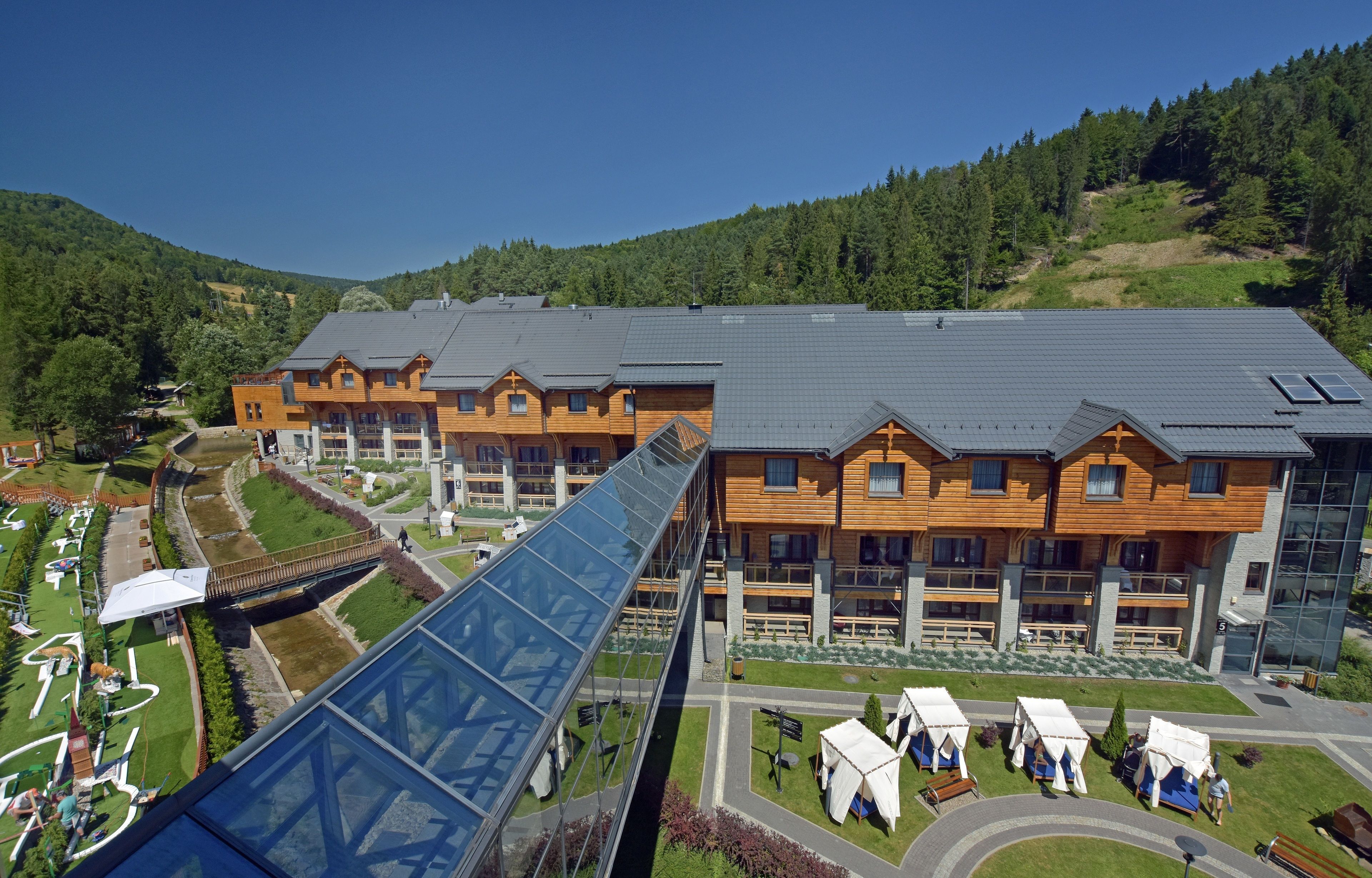 A modern hotel with multiple wooden buildings, a glass bridge, and outdoor seating areas.