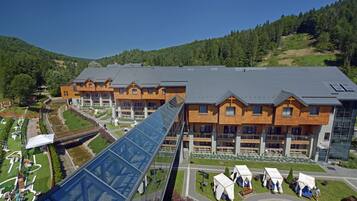 A modern hotel with multiple wooden buildings, a glass bridge, and outdoor seating areas.