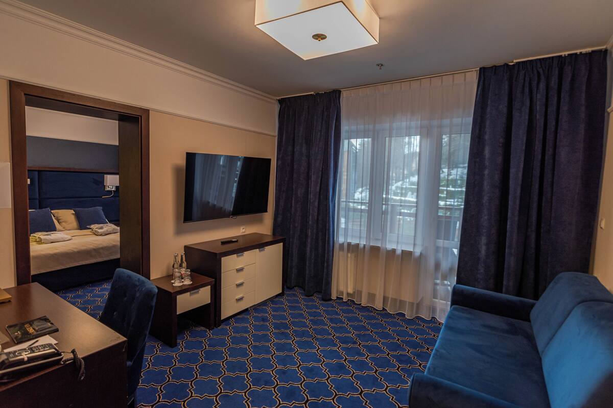 Una habitación de hotel con cama, escritorio, televisor, sofá y ventana con cortinas.