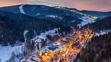 Vila coberta de neve com edifícios iluminados e uma pista de esqui ao fundo.