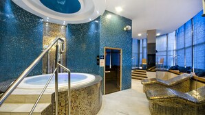Un área de piscina interior moderna con un jacuzzi circular, una escalera con barandas de metal y zonas de estar con sillas de mimbre.