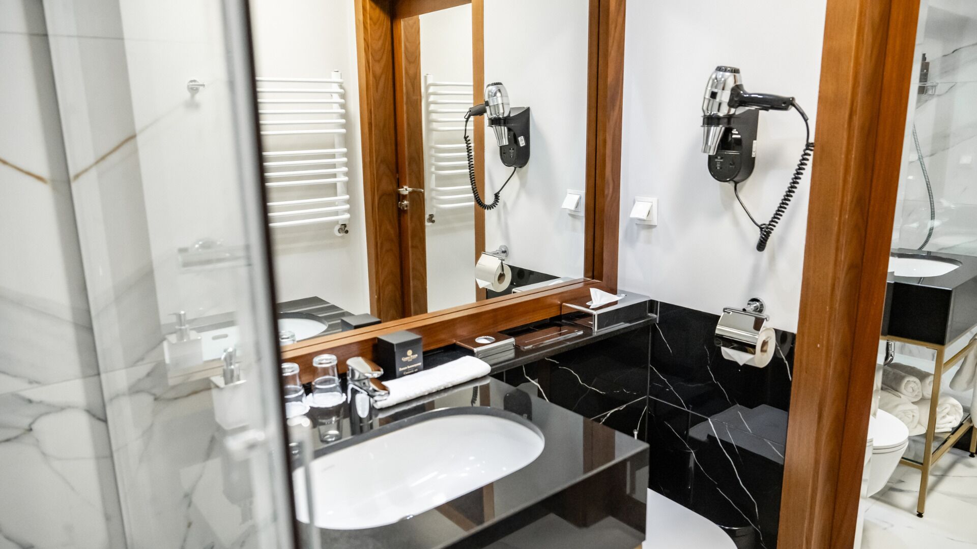Un baño moderno con un espejo grande, un lavabo negro y dos secadores de pelo montados en la pared.